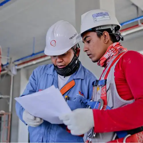 Two construction workers reviewing blueprints indoors.