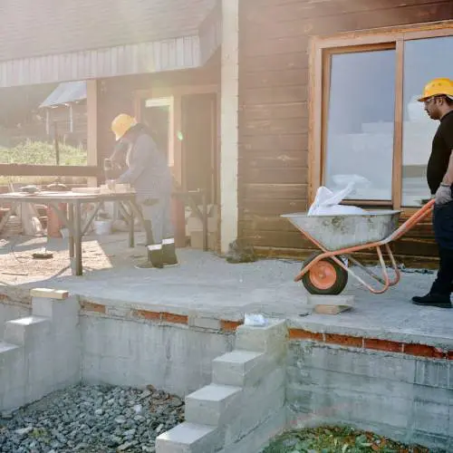 Construction workers with wheelbarrow outside building.